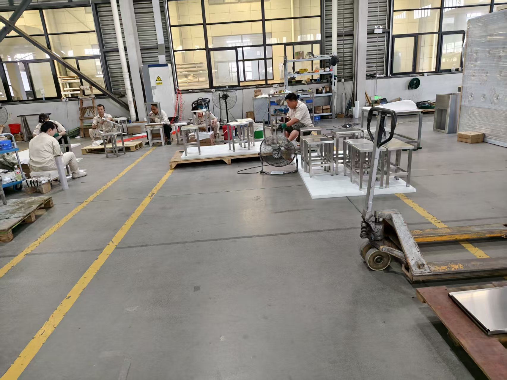 Workers and metal frames beside work surfaces and pallets in a workshop